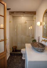 The stone floors are continued in here, with a smaller natural stone mosaic on the shower floor. Waterproof stucco covers the shower and the vanity, now with unlacquered brass fixtures to encourage patina, and a stone vessel sink.