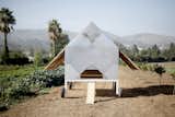 Its door automatically opens at dawn and closes at sunset, so the chickens can hop out and roam the land. The wings at the sides open to provide shade. The shingles are aluminum.
