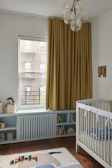Farrow &amp; Ball’s Hazy covers the custom millwork in this child’s room. “This is a very small room, which is typical to a lot of brownstones in Brooklyn,” says Cuttle. “You have this very narrow space and you're trying to make the most of it. So, the built-in stretches the length of that wall and gives the illusion of it being longer. Then the drapery reinforces the ceiling height.”