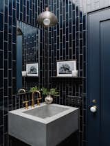 Walls are covered in Fireclay tile in Navy Blue. The vanity has a custom concrete basin by Newbold Stone Architectural Concrete and steel base from Metal Works Austin. The custom steel shelf and steel-edged mirror are paired with a perforated pendant by Allied Maker.