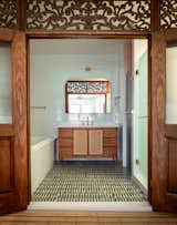 The shower and toilet are tucked in their own enclosures, so the doors can be left open to frame the custom vanity, which was designed to have the same wood tones as the screen but not compete. The flooring is Tappeti Green Blend Mosaic from Artistic Tile.