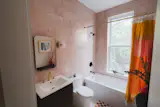 The 8x8-inch glossy pink tile in the Dolly bathroom was sourced at Rye Ridge Tile, with Edie prismatic sconces from West Elm, and a vanity and medicine chest found on Wayfair.