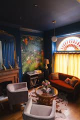 The cowhide rug was purchased on a road trip in Santa Fe, New Mexico, while the orange settee and rattan coffee table were found on Facebook Marketplace, the latter via @modastudiojc. Ellie Deneroff painted the "jungle