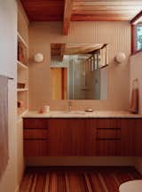 The vanity has a walnut base with an Arabescato Marble counter. A mirror is inset to be flush with the Umi Torimu tile, in Oat Glossy from DDS Tile.