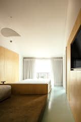 The architects designed a central unit with a built-in bed, and lounge just behind that, on the carpeted platform. A walk-in-closet area is unseen, at the other end of the room. Plywood covers the walls, and the original vaulted ceilings were painted white.