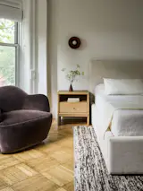 The primary bedroom has a Nerja rug by Ben Soleimani, Selki swivel chairs by Lulu &amp; Georgia, and Augustine wall sconce by Rejuvenation.