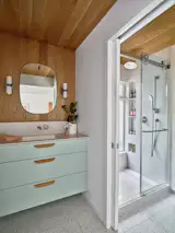 The flooring throughout the bathroom is Artistic Tile, in Venezia Terrazzo White. Wood paneling on walls and ceiling is more Rummer appropriate, with a Blu Dot mirror and In common with sconces. The vanity has Linear Standard pulls.