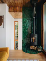 The pine boards continue on the ceiling in the stairwell. Green zellige tile forms a nook for the freestanding fireplace.