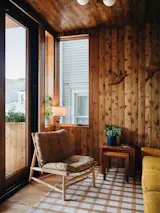 Scholtens incoporated the porch into the finished space as a family room, and covered walls and ceiling in knotty Pine panelling, as a callback to the previous porch. The couple's golden sofa tipped off Spot Lab that yellow was a favorite color, while the lamp in the corner was kept from the downstairs Tiki bar. The wooden birds came with the house.