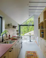 Kitchen, Cooktops, Dishwasher, Wood Cabinet, Drop In Sink, Cork Floor, Refrigerator, Ceramic Tile Backsplashe, and Recessed Lighting The cabinetry throughout is a mix of Ikea inserts and custom units. Additional blue accents include the structural collar ties, the table lamp, and the cabinet hardware.