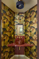 A <a href="https://concrettidesigns.com/products/key-west?variant=39470134886488">Concretti Designs</a> sink sits on a counter with <a href="https://www.fireclaytile.com/">Fireclay Tile</a>. A ceiling light from <a href="https://www.lumens.com/">Lumens</a> hangs above, while <a href="https://www.zoffany.design/wallpaper/abstract-1928-antique-copper-zow0084-02#details">Zoffany</a> wallpaper covers the walls. The mirror is from <a href="https://www.dwr.com/">DWR</a>.