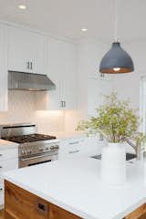 Fresh white kitchen with warm wood wrapped island, black cabinet pulls and Dwell patterns Heath tile backsplash .