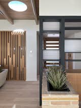 The partition visually separates the entry and dining room. The original brick planter was retained and round skylights were added to the ceiling, helping to balance the natural light and bring curves to an otherwise orthogonal design. A "haiku" screen on the left hides a hallway.