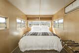 Bedroom, Bed, Wall Lighting, and Carpet Floor Interior of trailer.  The Rambler is now a clean, sleek retreat.  Photos from This Modern Homestead With a Vintage Trailer Offers Adventure in California's High Desert