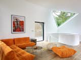 Designed by Atelier Du Pont, this breathtaking property exists in harmony with the surrounding landscape. Oriented in a manner that creates minimal impact on the existing terrain, the house idyllically nestles into nature, with vast views of the encompassing trees and vegetation. Inside, an orange Ligne Roset Sofa provides a comfortable space for rest and relaxation. A triangular window provides a picture of the tree canopy beyond, while drawing in natural light.