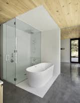 Bath, Enclosed, Ceramic Tile, Concrete, Freestanding, and Ceramic Tile White, hexagon tiles frame a shower and bath block of space in the Master Bath.   Bath Ceramic Tile Concrete Enclosed Photos from This Wood-Clad Home Is Built Into a Serene Mountain Slope