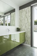 Glossy green cabinets, textured wall coverings, and polished concrete floors in desert hues decorate one of the guest baths. 