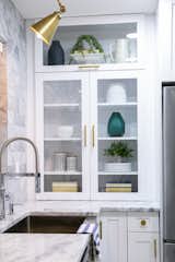 White shaker cabinets, some with glass inserts, combined with brass knobs and pulls, are a modern uptake on a simple style. 