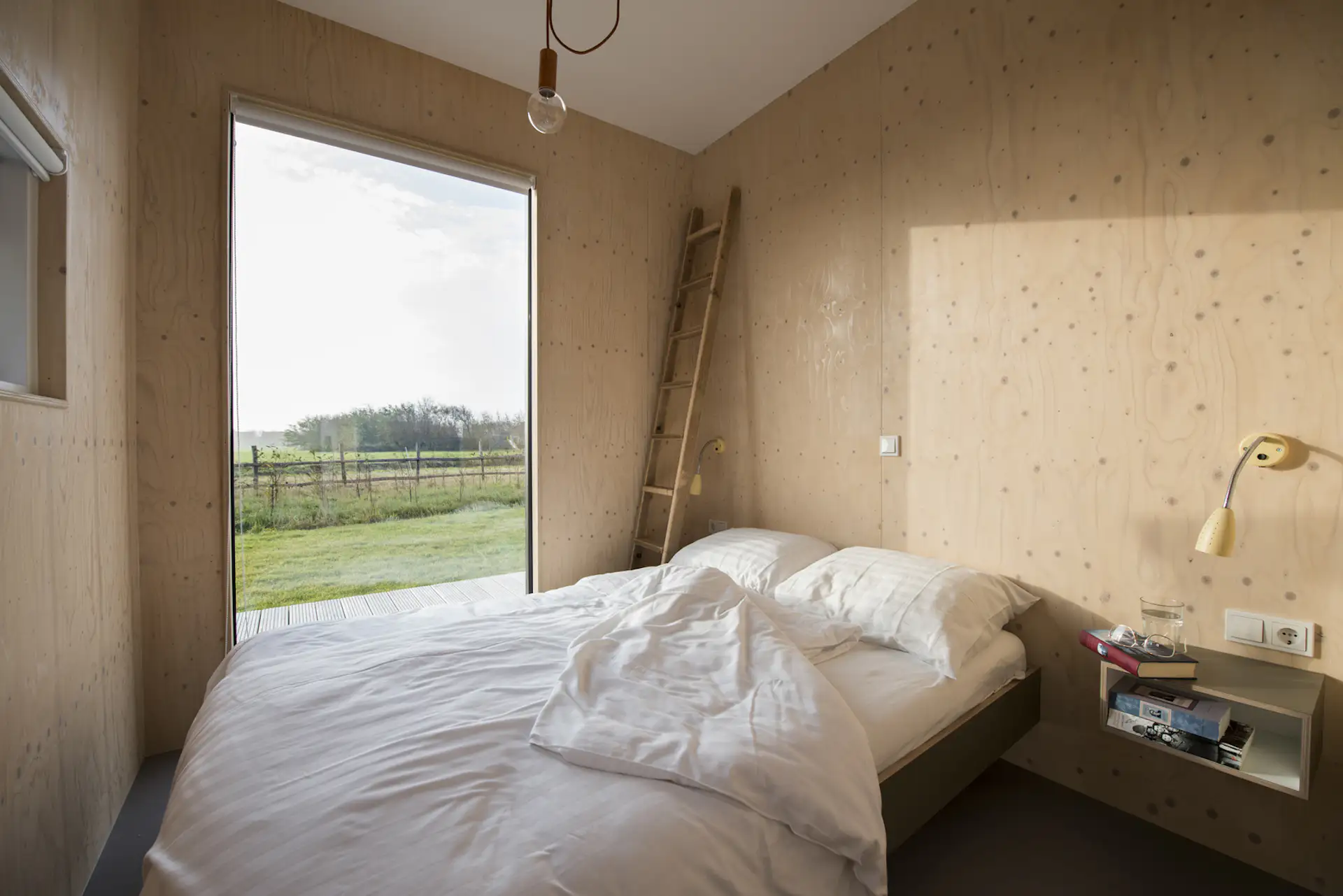 Bedrooms are adorned with the same simple material palette. Wood-clad walls, white ceilings, large windows, and simple pops of color allow the views to remain the focal point.