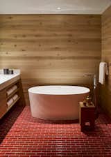Rustic meets modern.  An elegant soaking tub pops against the natural wood and deep red tiles in one of the en-suite baths. 