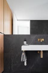 Minimal and sleek finishes decorate the bath interiors.  Gold hardware is a rich element that pops against the dark tiled walls. 