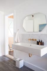 Brass and marble accents, a large wall-mounted sink, and a geometric mirror create a serene bath retreat.