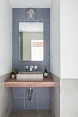 The main floor bathroom was reduced in size to accommodate the new kitchen pantry. The three-quarter bath includes a custom floating walnut slab vanity, dark blue linen-textured tiles, and chrome accents.