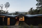The folded metal roof plane provides protection to the home's entryway while framing the view through the home’s dining area to the lush hills beyond.