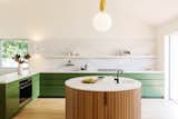 Courtyard House by And And And Studio kitchen with green cabinets, marble countertops, and a round island