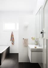 A full bathroom now fills part of the original living space. Dark Fiandre floor tiles contrast with a mix of bright white matte and gloss wall tiles. A Glo Ball wall sconce from Flos is the perfect playful addition to this modern bath.