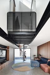 A spiral staircase leads to a bathroom and three bedrooms above. A perforated steel landing connects the bedrooms above and bridges a double-height main living space. 