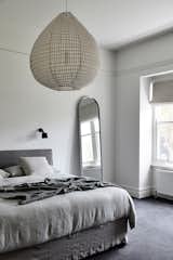 The bedrooms are located in the more private front of the home. The original trim, windows, and casing remain, paired with modern furnishings and textiles. Here, a large decorative pendant light from Hub Furniture and a rounded floor mirror from Biasol Design serve as subtle accents. 