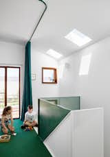 A flexible loft space at the top of the stairs doubles as a sleeping area when the curtain is closed, and a playroom for the kids. Skylights and punched window openings allow natural light to filter into these upper-level living spaces