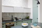 In the kitchen, lemon-yellow and mint-green cabinets complement the forest-green granite countertops. White overhead cabinets blend in with the white brick backdrop.