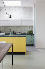 Colored wall cabinets and a kitchen island structure the open-plan cooking area. White-painted bricks and a large skylight keep the space bright.