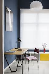 Simple office furniture in primary colors stands out against marine-blue walls and a white window shade.