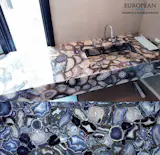 This bathroom countertop design features Agatona from our Precioustone collection. A selection of large and precious gem-size agate pebbles are sliced by diamonds to show their natural silver-grey color off to best effect. 
Each of these slabs is made up with specially selected specimens of Agatona which have been painstakingly laid out and hand-assembled to take full advantage of translucent qualities of agate. It is suitable for all indoor applications.

More info here: http://www.egmcorp.com/precioustone-collection/agatona
