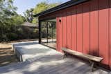 Detail of red standing seam metal siding with bench at raised deck and corner sliding door unit