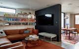 Family Room with bookshelves and a television disguised on the charcoal cement plaster wall that slips by the dining table sliding door beyond.  This space opens onto the kitchen and dining and acts as a catchall gathering room to lounge before and after meals.