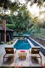 Outdoor, Grass, Lap Pools, Tubs, Shower, Shrubs, Side Yard, Garden, Wire Fences, Wall, Back Yard, Trees, Small Patio, Porch, Deck, Retaining Fences, Wall, Standard Construction Pools, Tubs, Shower, Landscape Lighting, Gardens, Concrete Patio, Porch, Deck, Decking Patio, Porch, Deck, Wood Patio, Porch, Deck, Hardscapes, Swimming Pools, Tubs, Shower, and Small Pools, Tubs, Shower The lounge deck at the rear yard of Sunset Hills Residence features a swimming pool surrounded by lush gardens. Architect Hsu McCullough's design beautifully merges minimalism with an abundance of nature.  Photo 3 of 5 in Top 5 Homes of the Week With Eye-Popping Pools from Sunset Hills Residence