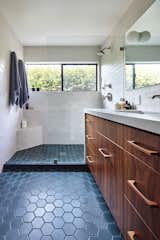 Bathroom with American black walnut cabinetry including walnut cabinet pulls with tile from Mission Tile West. Tiered levels of tiled horizontal surfaces in the shower form the soap/shampoo shelf along with a small corner bench. A denim-colored hexagon tile extends from the wet area through to the vanity. As per the rest of the house, windows open to the garden beyond.