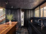 Wood siding of the exterior wraps into the house at the south end of the kitchen concealing a pantry and panel-ready column, Fisher&Paykel refrigerator and freezer as well as a coffee bar. An assemblage of textures and raw materials including a dark-hued, minimalist layout for the kitchen opens to living room with panoramic views of the canyon to the left and the street on the right. We dropped the kitchen ceiling to be lower than the living room by 24 inches.  There is a roof garden of meadow grasses and agave above the kitchen which thermally insulates cooling the kitchen space.  Soapstone counter top, backsplash and shelf/window sill, Brizo faucet with Farrow & Ball "Pitch Black" painted cabinets complete the edges. The smooth stucco of the exterior walls and roof overhang wraps inside to the ceiling passing the wide screen windows facing the street.An American black walnut island with Fyrn counter stools separate the kitchen and living room over a floor of black, irregular-shaped flagstone. Delta Light fixtures were used throughout for their discreet beauty yet highly functional settings.