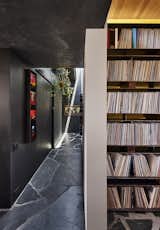 Record shelves lead to a gallery hallway with a slot skylight running length of the space. A hanging container garden of Pothos, Philodendrons and other indoor plants benefit from the natural light. A laundry room sits behind the rolling barn door clad in black burlap.