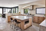 Tiled kitchen with birch cabinetry opens to outdoor dining beyond windows. Entry with stair to second floor and dining room.