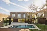 Widespread chevron-shaped rear yard facade with detached pool house ADU, swimming pool, spa, raised wood deck, lawn and concrete patio. Home is designed to bend around existing 50-foot tall elm tree