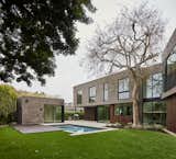 Widespread chevron-shaped rear yard facade with detached pool house ADU with garden roof, swimming pool, spa, raised wood deck, lawn and concrete patio. Home is designed to bend around existing 50-foot tall elm tree