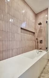 A children's bathroom with pink Fireclay tile and combination tub shower clad in engineered quartz. Carefully coordinated wall recess for shower gels and soap 