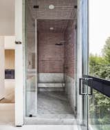 A deeply set steam shower at the primary suite features a cantilevered Carrara marble slabs bench and wainscott as well as pink Fireclay tile. Large window frames yard beyond.