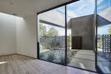 Enclosed entry courtyard of breeze block, smooth stucco walls and Thermory wood siding clad gate creates a private entrance from the street. As seen from the pivot door threshold. Portion of living at left with skylight above.