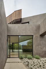nside enclosed entry courtyard of breeze block (seen in reflection) and smooth stucco walls marking a private entrance to a pivot door. Roof stair clad in Thermory wood siding above.